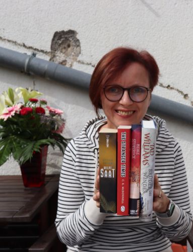 Evas Bücher-Herbst 2022 © Eva Bergschneider, Eva auf der Terasse, hält vier Bücher in die Kamera