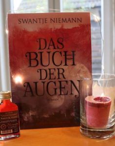 Das Buch der Augen - Swantje Niemann, Foto © Eva Bergschneider, Cover © Edition Roter Drache, Buch auf Esszimmertisch mit Met-Fläschchen und Kerze