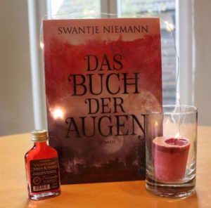Das Buch der Augen - Swantje Niemann, Foto © Eva Bergschneider, Cover © Edition Roter Drache, Buch auf Esszimmertisch mit Met-Fläschchen und Kerze