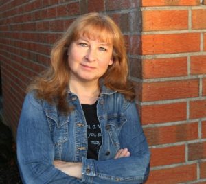 Jacqueline Montemurri © Jacqueline Montemurri, Portraitfoto, Jacqueline steht mit schwarzem T-Shirt und in Jeans-Jacke an der Hauswand